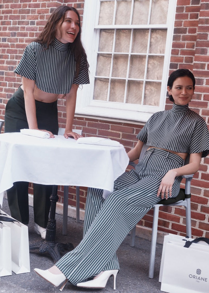 Two women in matching striped outfits sitting outdoors with shopping bags.